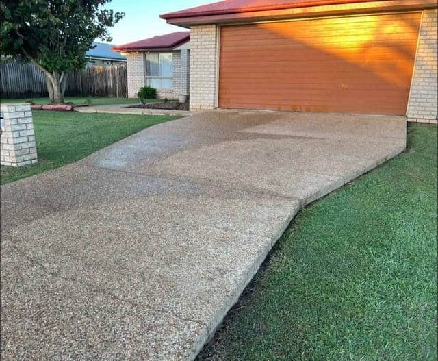 A driveway and garage in warm afternoon light beside a cut lawn