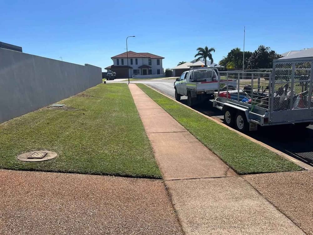 A ute and caged trailer parked at the kerb beside a freshly mown verge